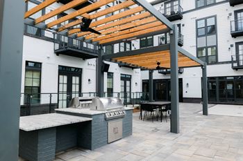 A patio with a grill and a table under a pergola.